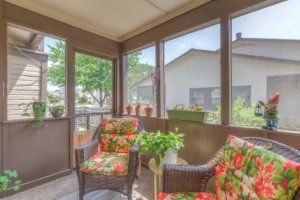 A cozy sunroom with wicker furniture, featuring floral cushions and potted plants, offering an inviting view of the outdoors.