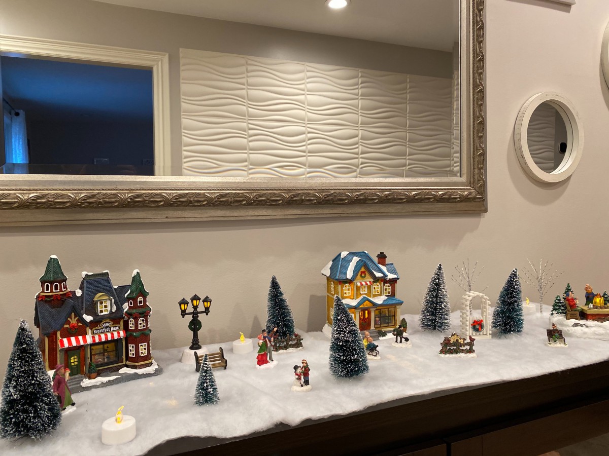 A festive miniature Christmas village display set in front of a large mirror.