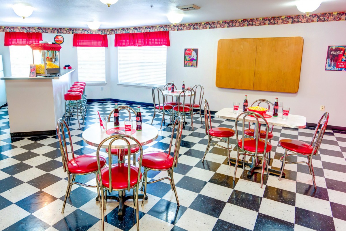 A vintage-style diner with red and chrome furniture, featuring a classic black-and-white checkerboard floor.