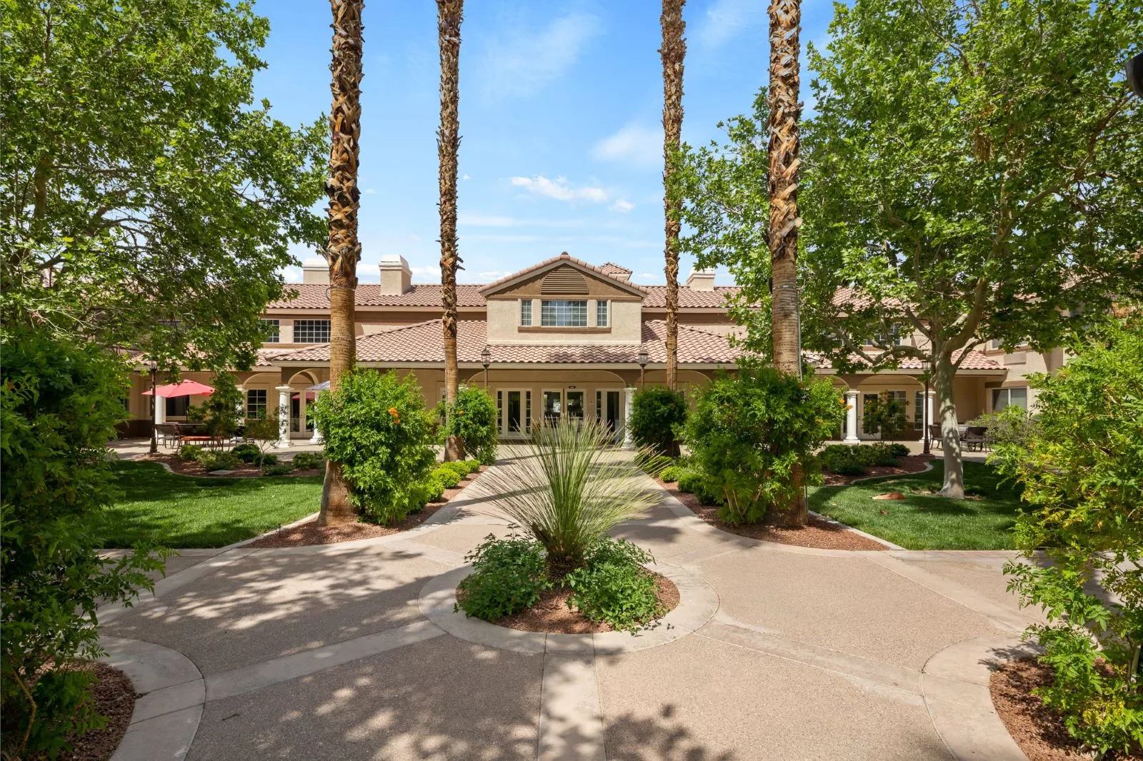 A grand mansion surrounded by palm trees and well-maintained gardens.