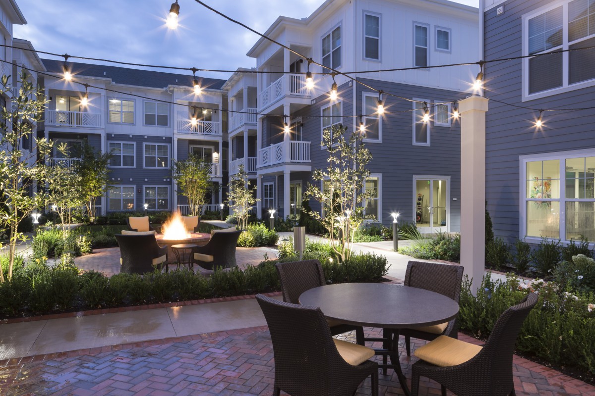 A cozy apartment courtyard with string lights and a firepit at dusk.