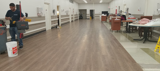 A spacious, well-lit interior room with a modern wooden floor and minimal furniture.