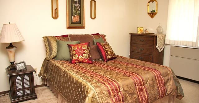 A traditionally styled bedroom with a richly decorated bed and matching pillows, accompanied by complementary wall art and wooden furniture.