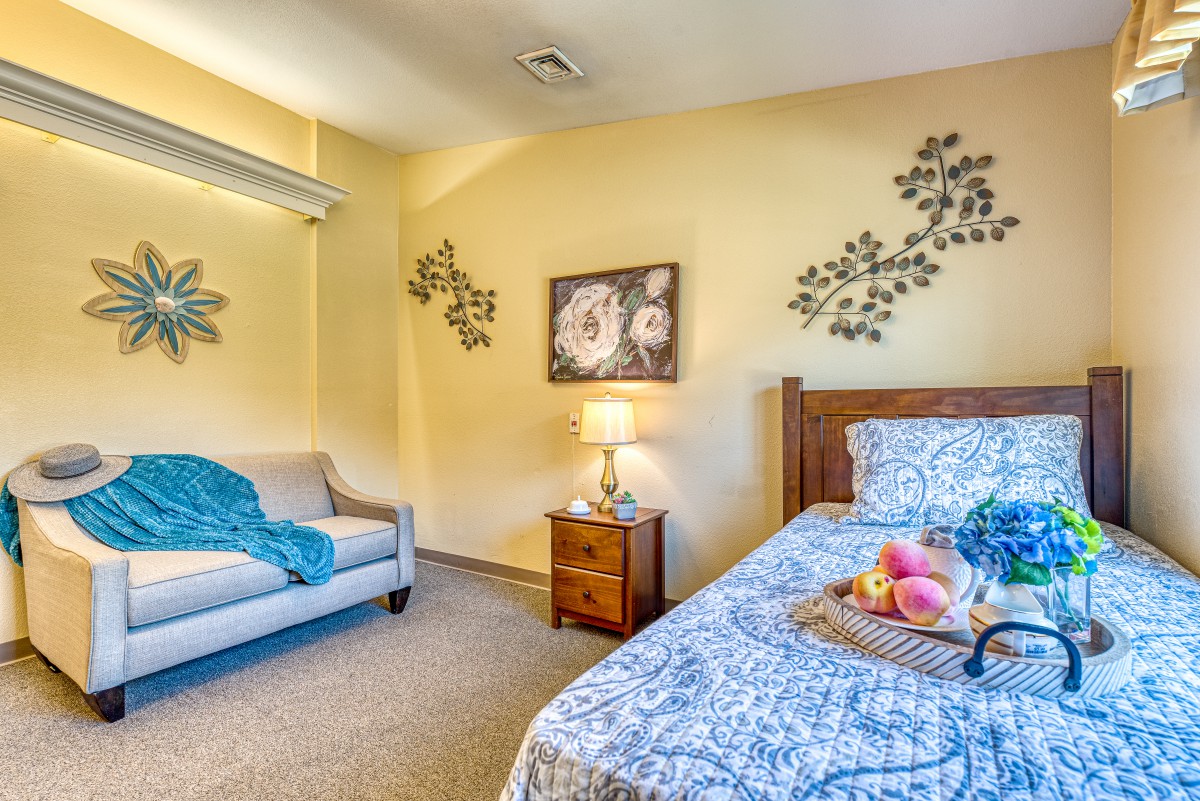 A cozy bedroom with a single bed, decorative wall art, and a small couch.