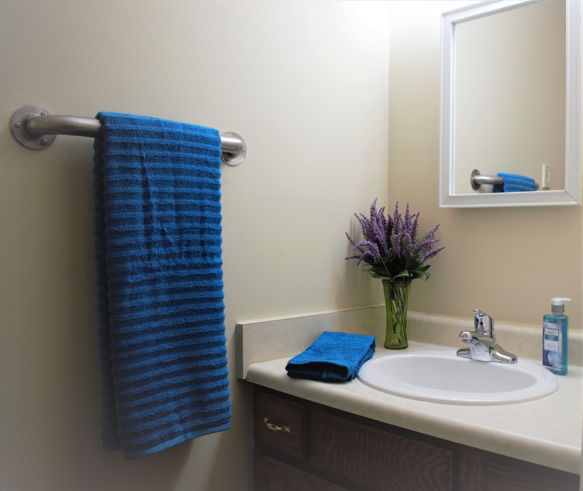 A neatly organized bathroom with a blue striped towel, a sink, and a vase of flowers on the countertop.
