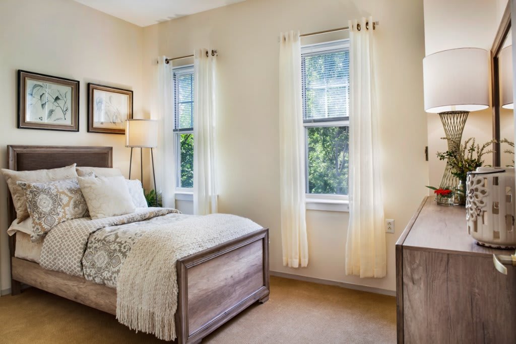A cozy bedroom with a single bed, light curtains, and natural lighting.