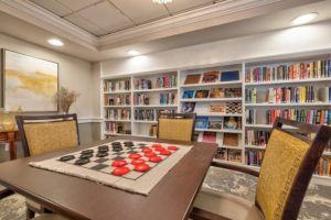 A cozy library with a checkers game set up on a table, surrounded by bookshelves.