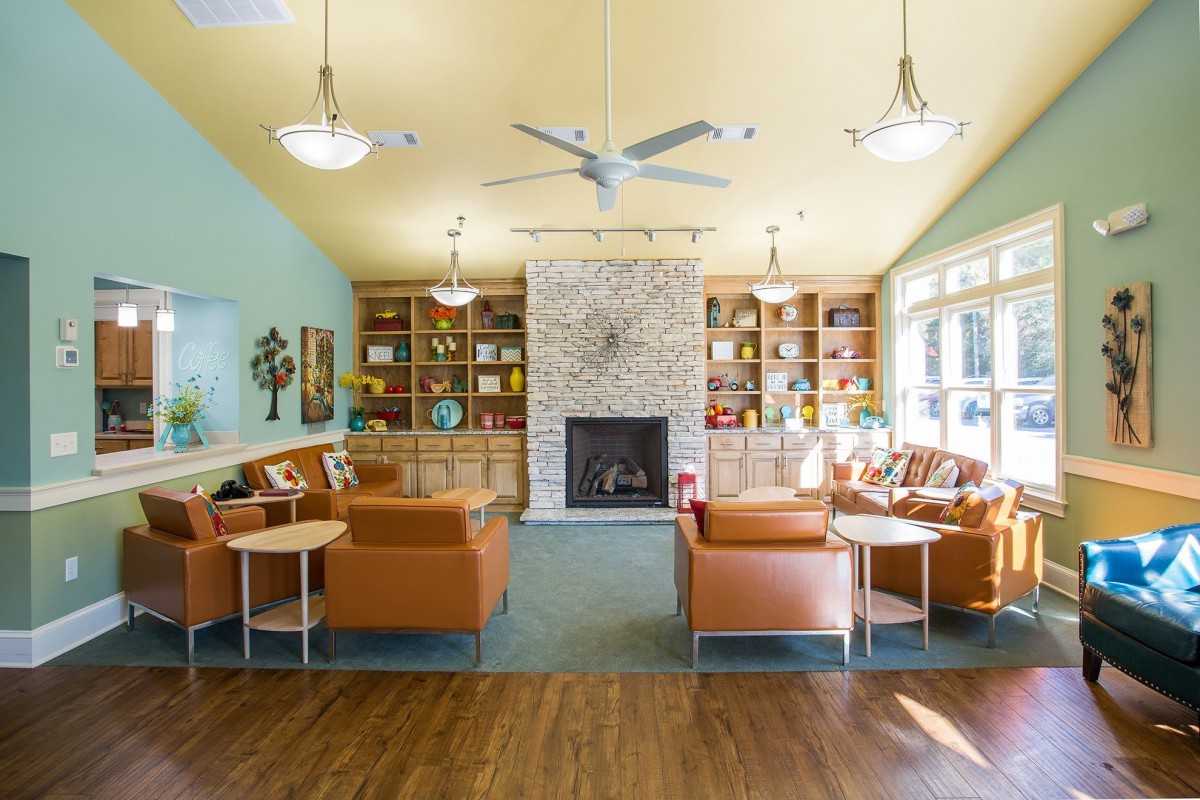 A cozy living room with a central fireplace, surrounded by bookshelves and ample seating, illuminated by natural light.