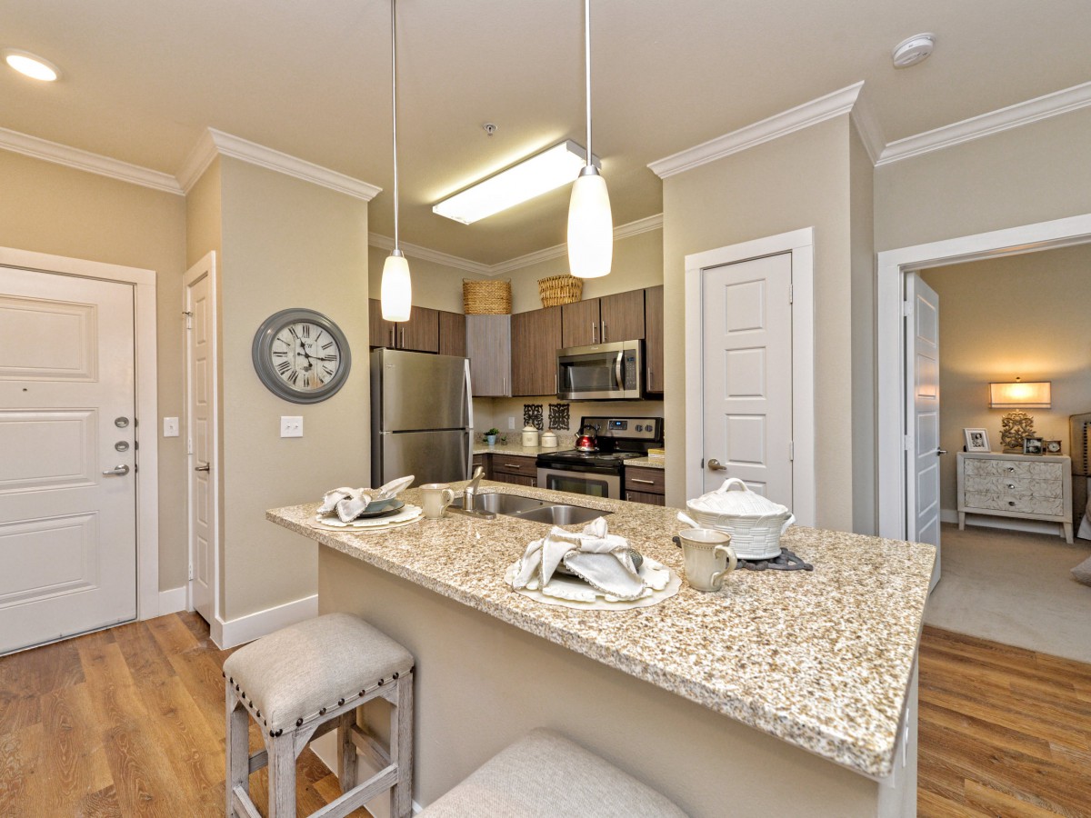 A modern kitchen with granite countertops and stainless steel appliances, featuring pendant lighting and bar stools.