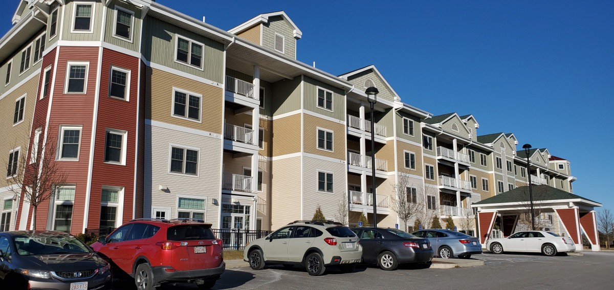A modern apartment building with several parked cars in front under a clear blue sky.