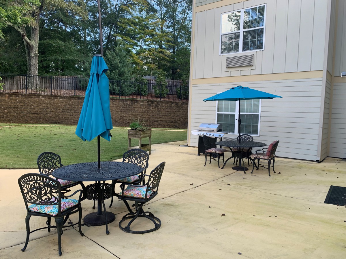 A backyard patio with tables, chairs, and umbrellas set up for outdoor seating.