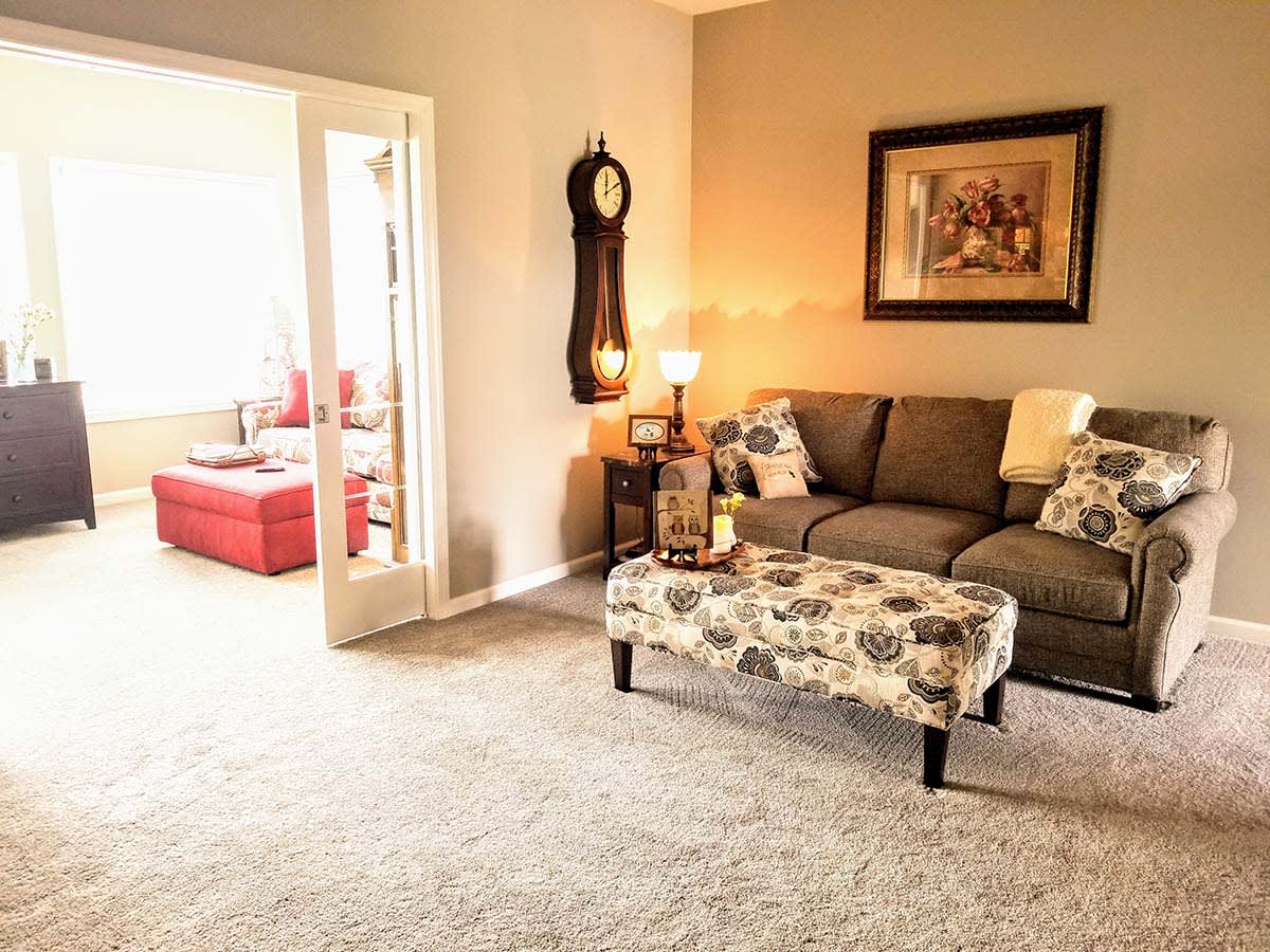 A cozy living room with a grey sofa, patterned ottoman, and soft lighting.