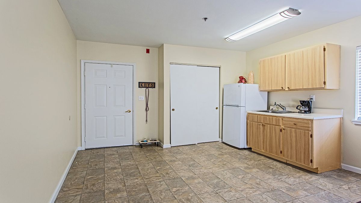 A kitchen area with a refrigerator, wooden cabinets, and a tile floor.