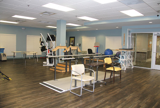 A spacious physical therapy room equipped with various exercise tools and chairs, designed for rehabilitation activities.