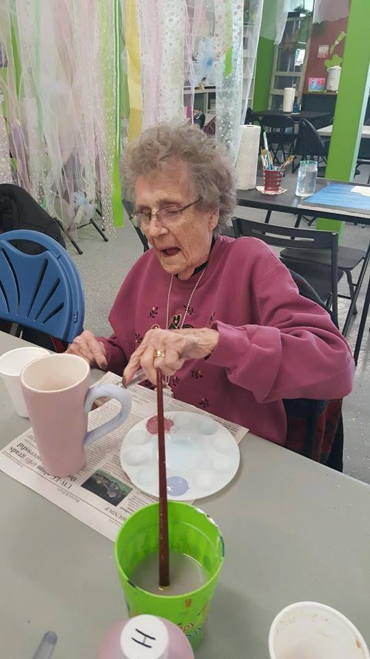 An elderly woman engaged in a painting activity at a table inside.
