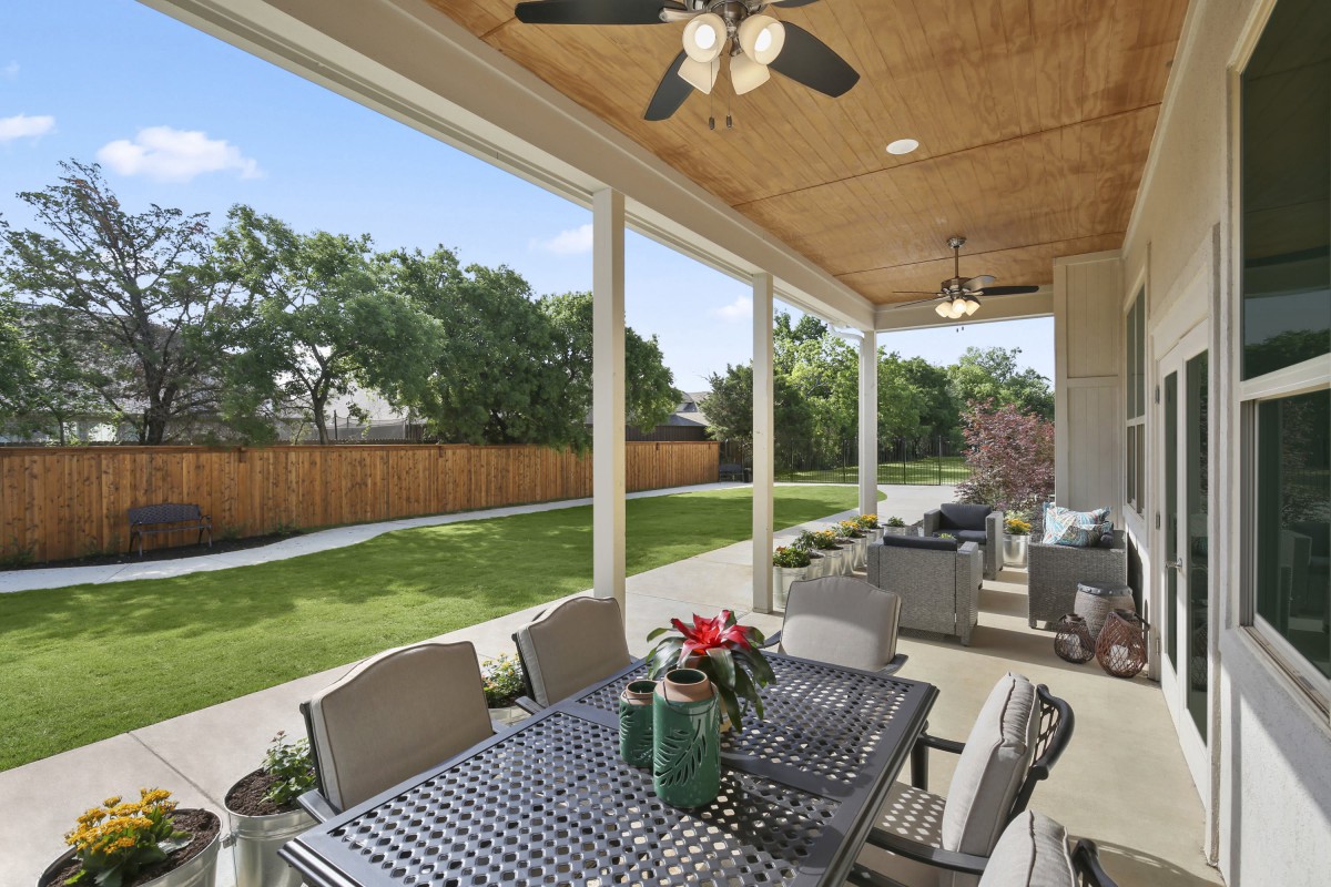 A cozy outdoor patio with a dining table, ceiling fans, and a view of the landscaped backyard.