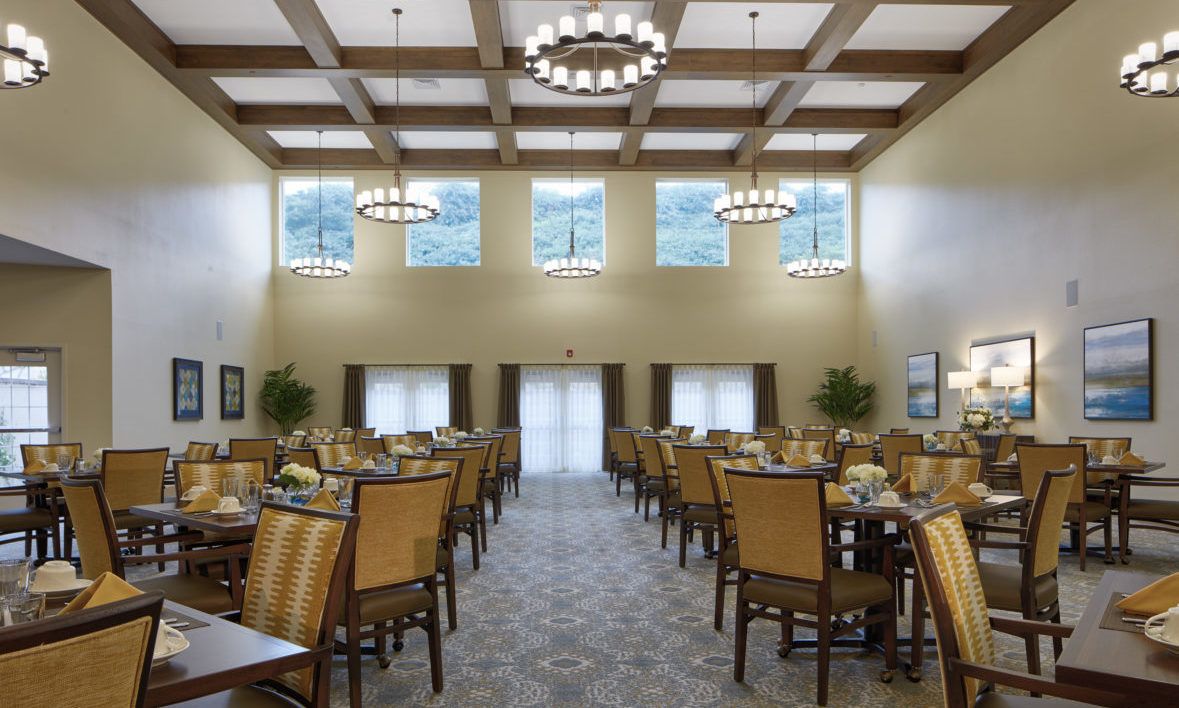 A spacious dining room with neatly arranged tables and chairs, illuminated by elegant chandeliers.