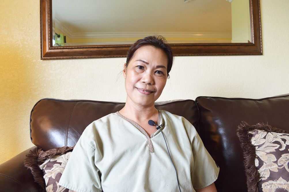 A person sitting on a couch indoors and smiling while wearing casual clothing.