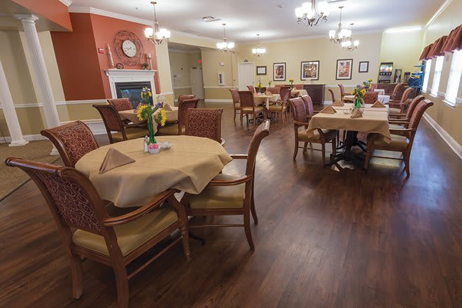 A neatly arranged dining room with wooden tables and chairs, decorated with flowers and soft lighting.