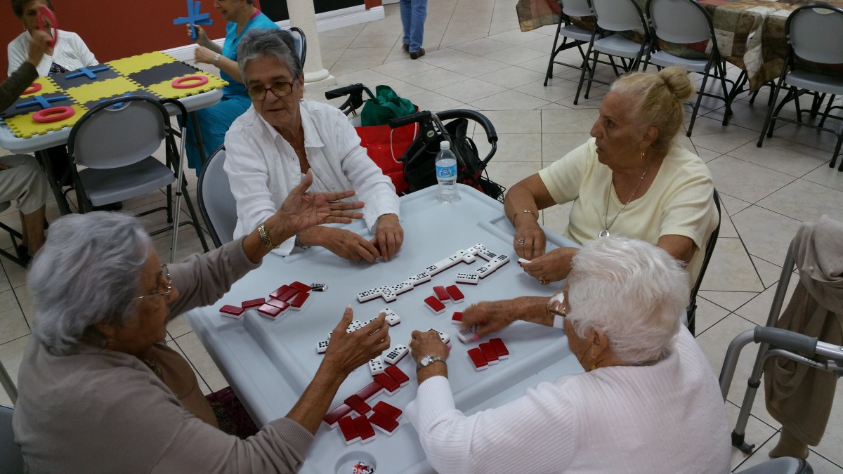A group of elderly individuals playing dominoes together at a table indoors.