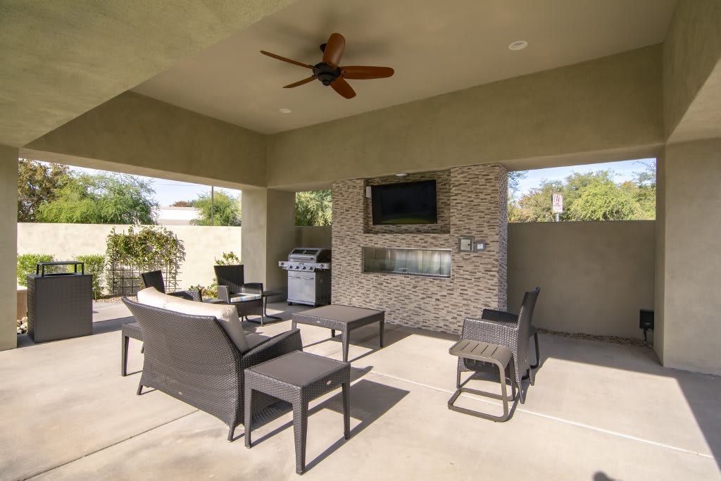 A spacious outdoor patio with comfortable seating, a TV, and a grill under a covered area.
