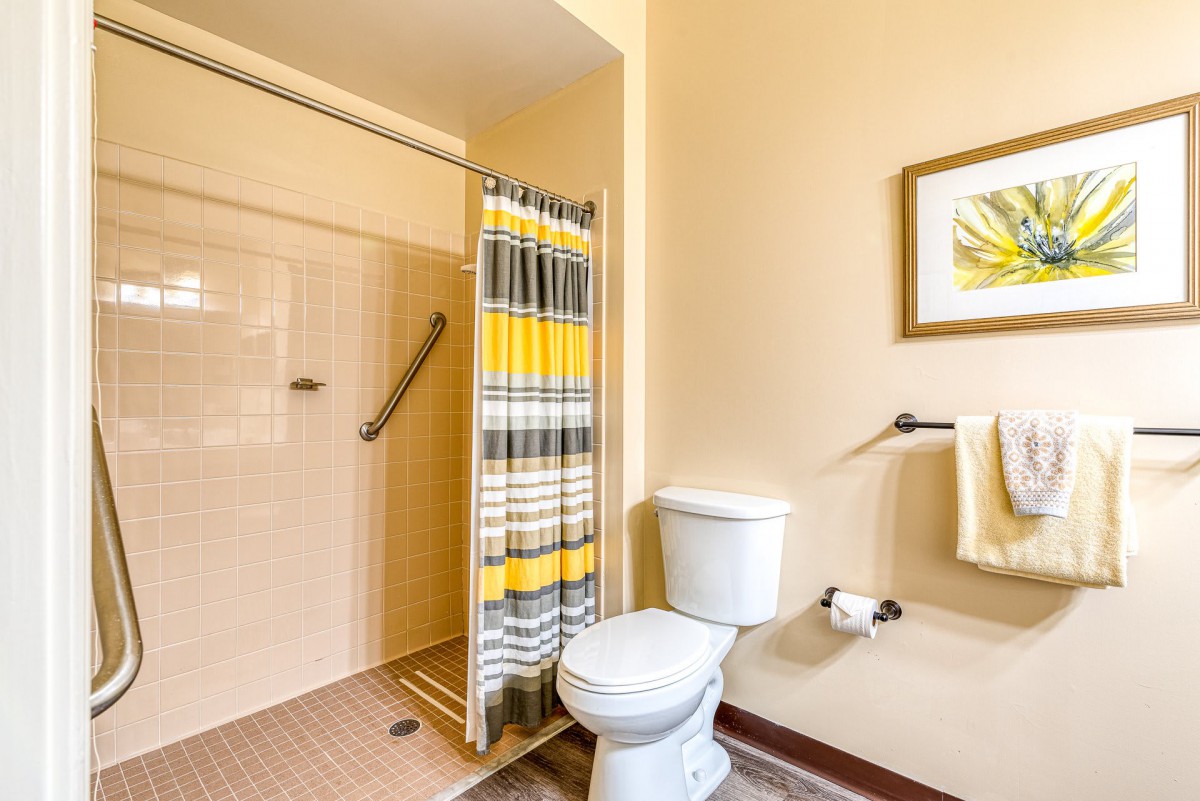 A clean and bright bathroom featuring a shower with a striped curtain, toilet, and neatly arranged towels.
