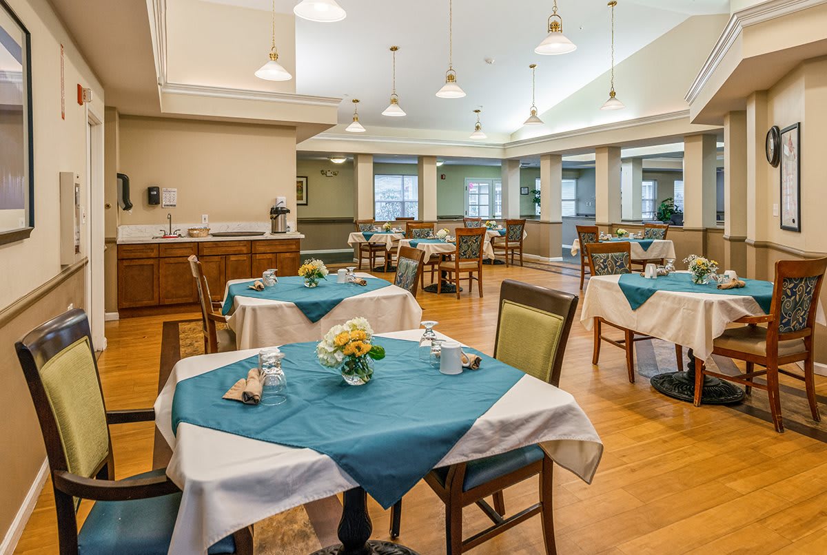 A well-lit dining room with neatly arranged tables and chairs, featuring blue and white tablecloths.