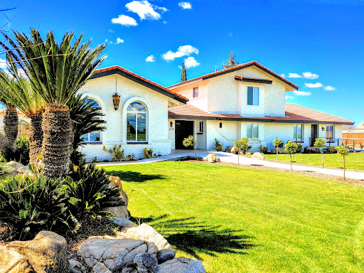 A beautiful residential home with a manicured lawn and palm trees under a clear blue sky.