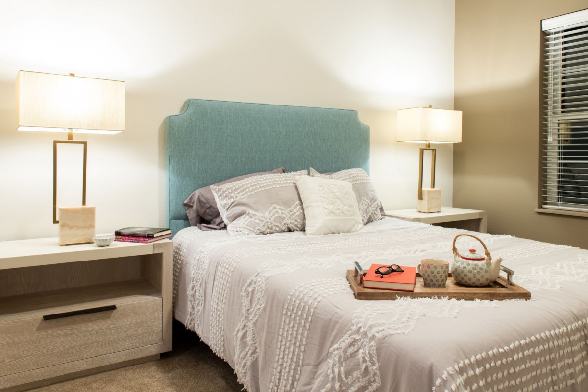 A cozy bedroom featuring a neatly made bed with a blue headboard, flanked by two nightstands and lamps.