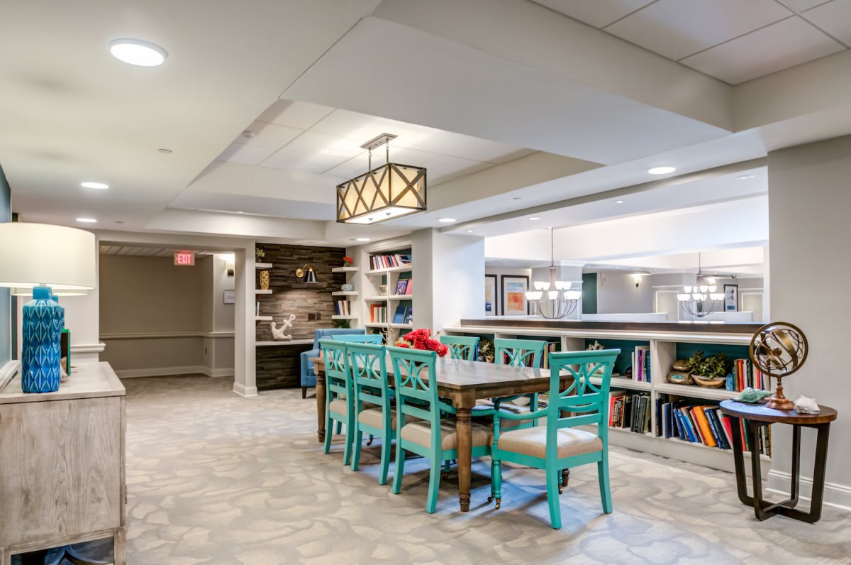 A modern dining area with teal chairs and a wooden table, surrounded by bookshelves and ambient lighting.