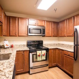 A modern kitchen with wooden cabinets and granite countertops, featuring stainless steel appliances.