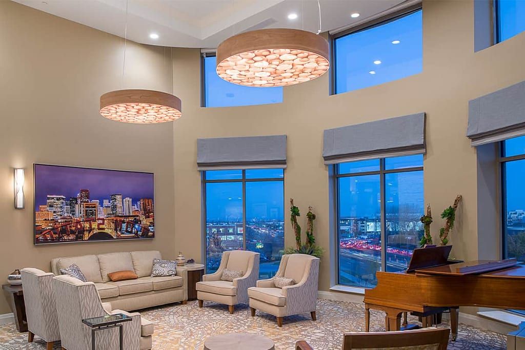 A modern living room with large windows offering a city view, featuring elegant furniture and stylish chandeliers.