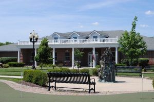 A scenic outdoor view featuring a building with a porch, surrounded by gardens and a fountain.