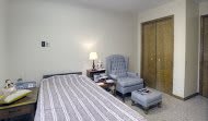 A cozy bedroom featuring a striped bed, comfortable chair with ottoman, and a wooden closet.