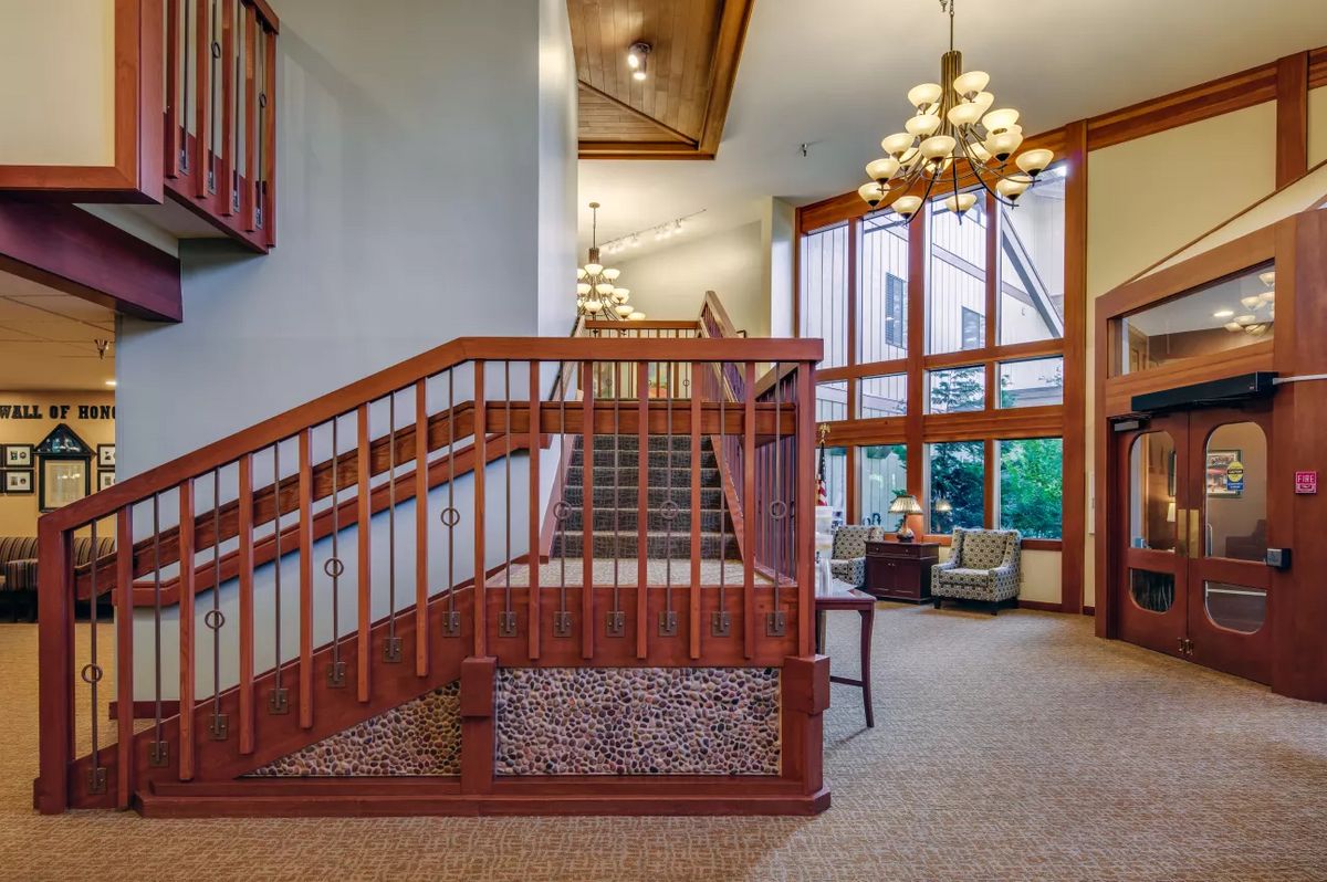 A cozy interior featuring a wooden staircase, chandelier, and large windows.