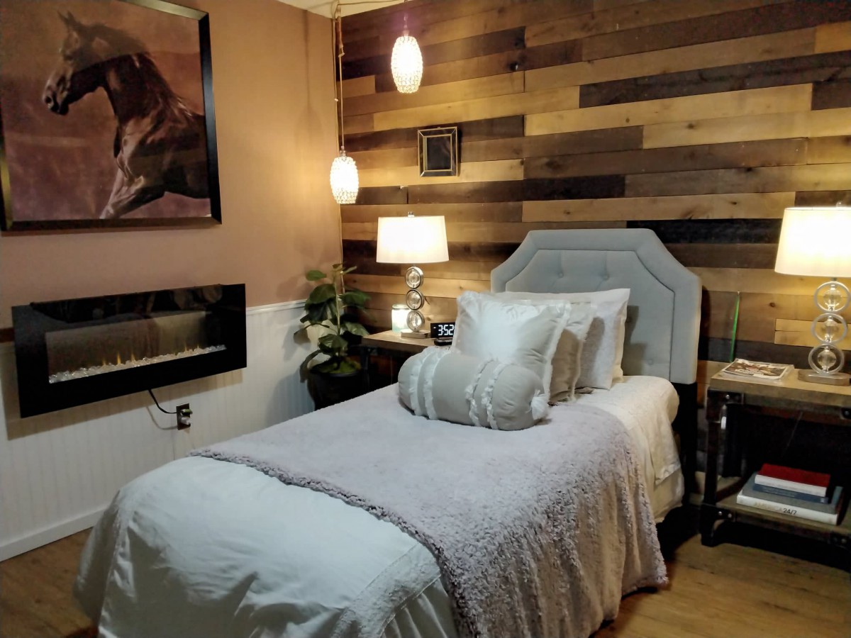 A cozy bedroom featuring a single bed with plush pillows and a wooden accent wall, softly lit by pendant lights.