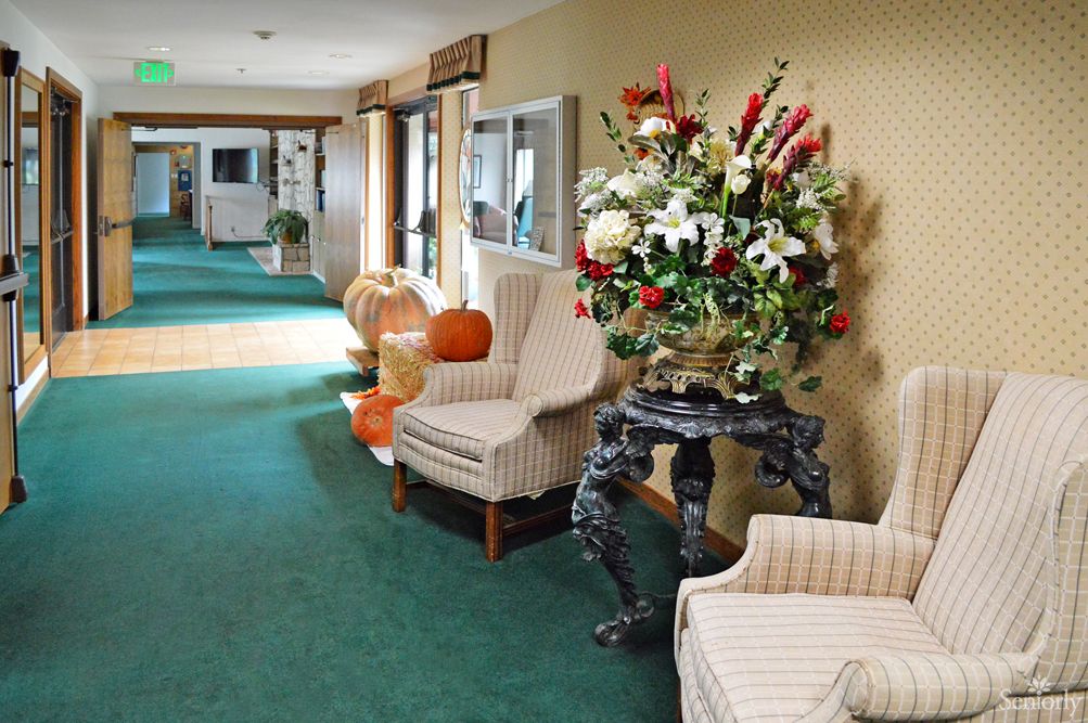 A decorated hallway with chairs, floral arrangements, and pumpkins.