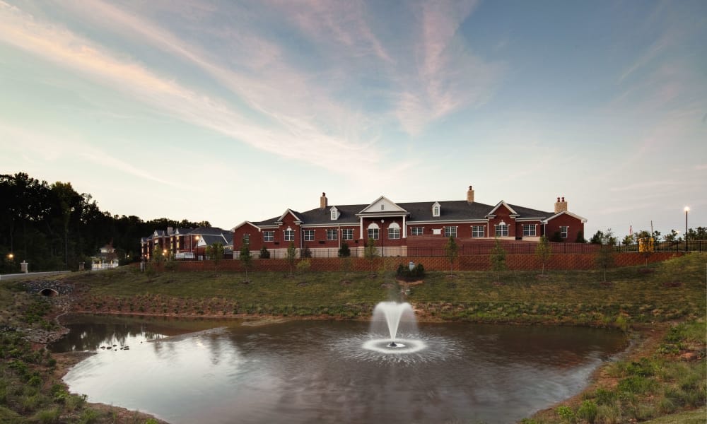 A large brick building with a fountain in a pond in the foreground under a colorful sky.