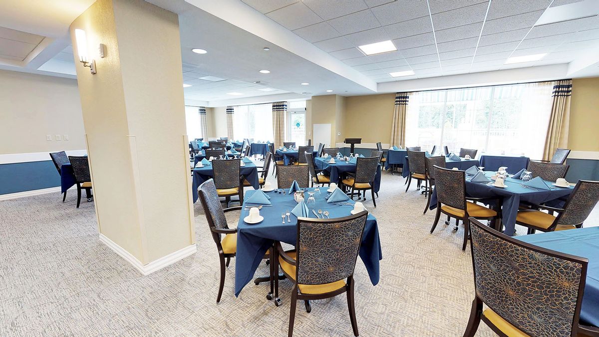 A spacious dining room with several tables set with blue tablecloths, ready for an event.