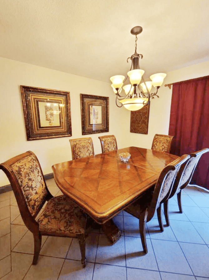 A well-appointed dining room with a wooden table and upholstered chairs beneath a decorative chandelier.