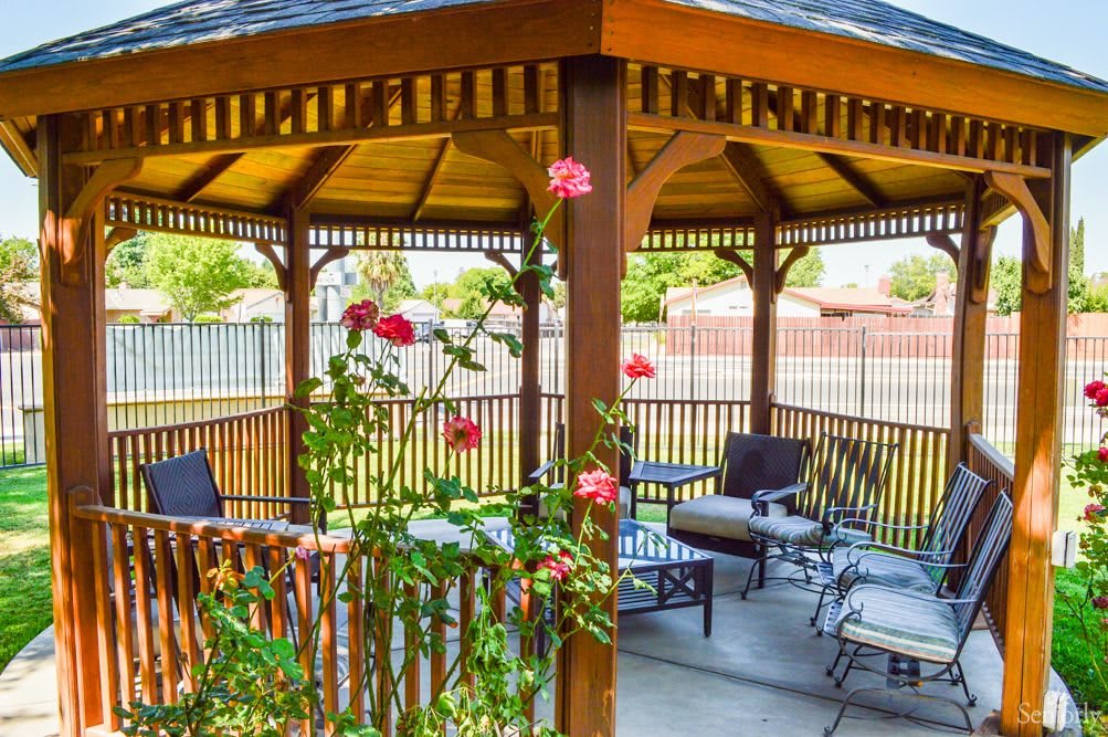 A cozy gazebo with comfortable seating surrounded by a garden of vibrant flowers.