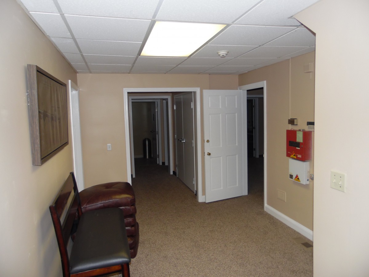 An interior view of an office hallway with multiple doors and a bench.