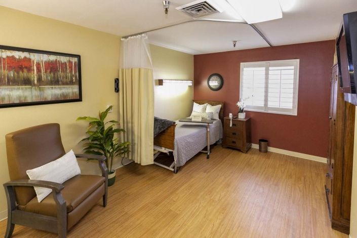 A well-furnished hospital room with a bed, chair, and decorative items.