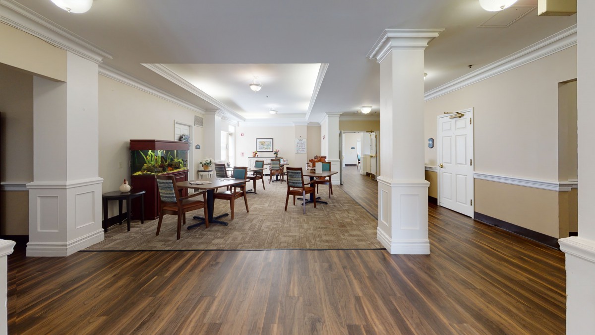A spacious and well-lit dining area with wooden flooring and neatly arranged tables and chairs.