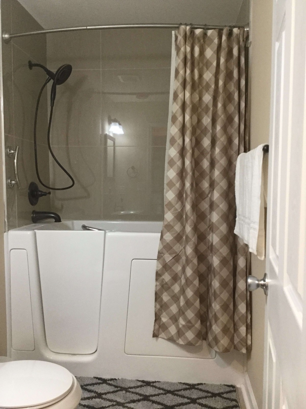 A bathroom featuring a walk-in bathtub with a shower curtain and a towel hanging on the door.