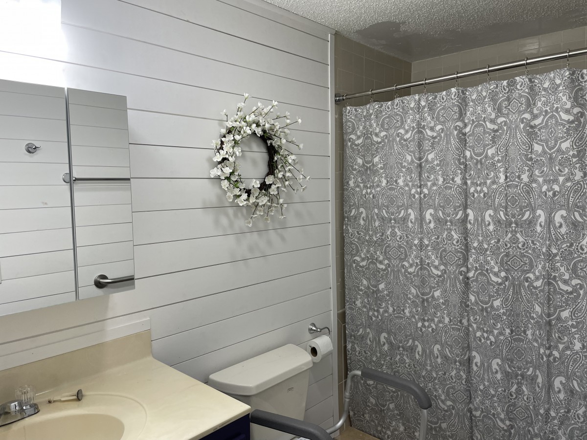 A clean, modern bathroom with a floral wreath on the wall and a patterned shower curtain.