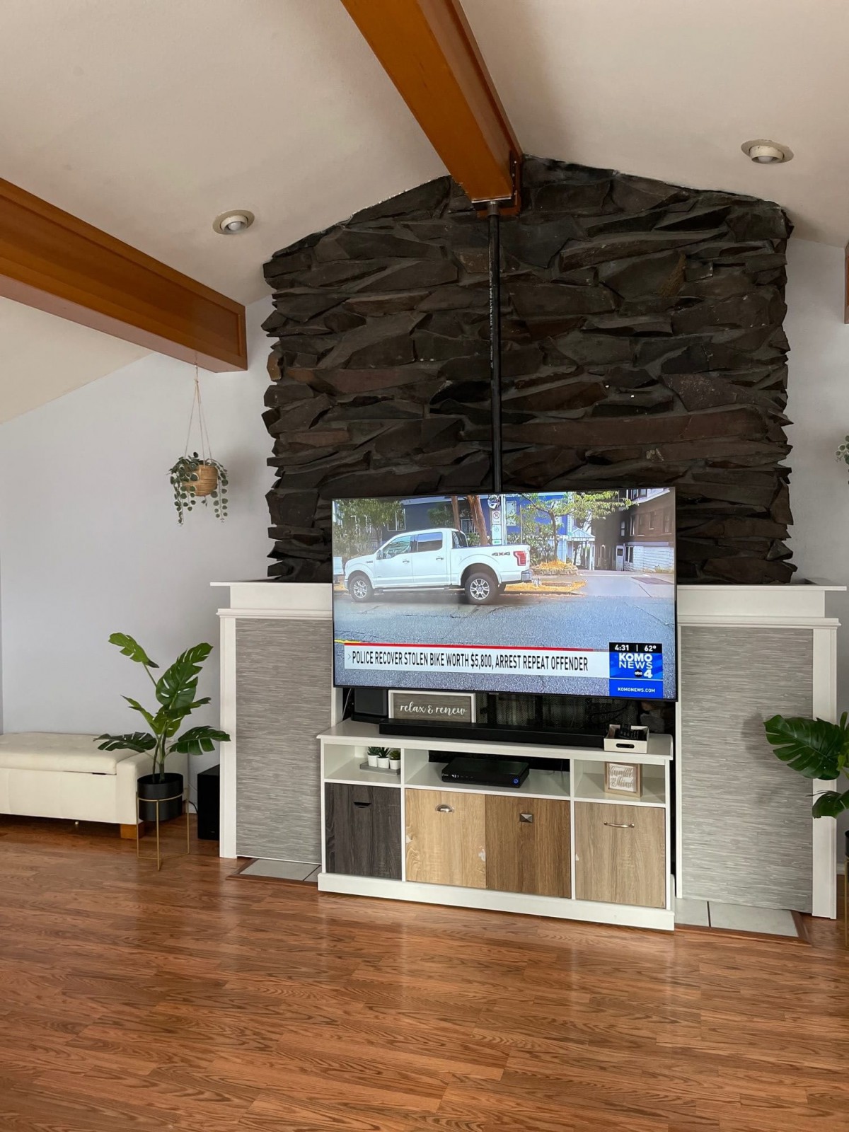 A modern living room with a mounted television above a fireplace, featuring wood flooring and decorative plants.