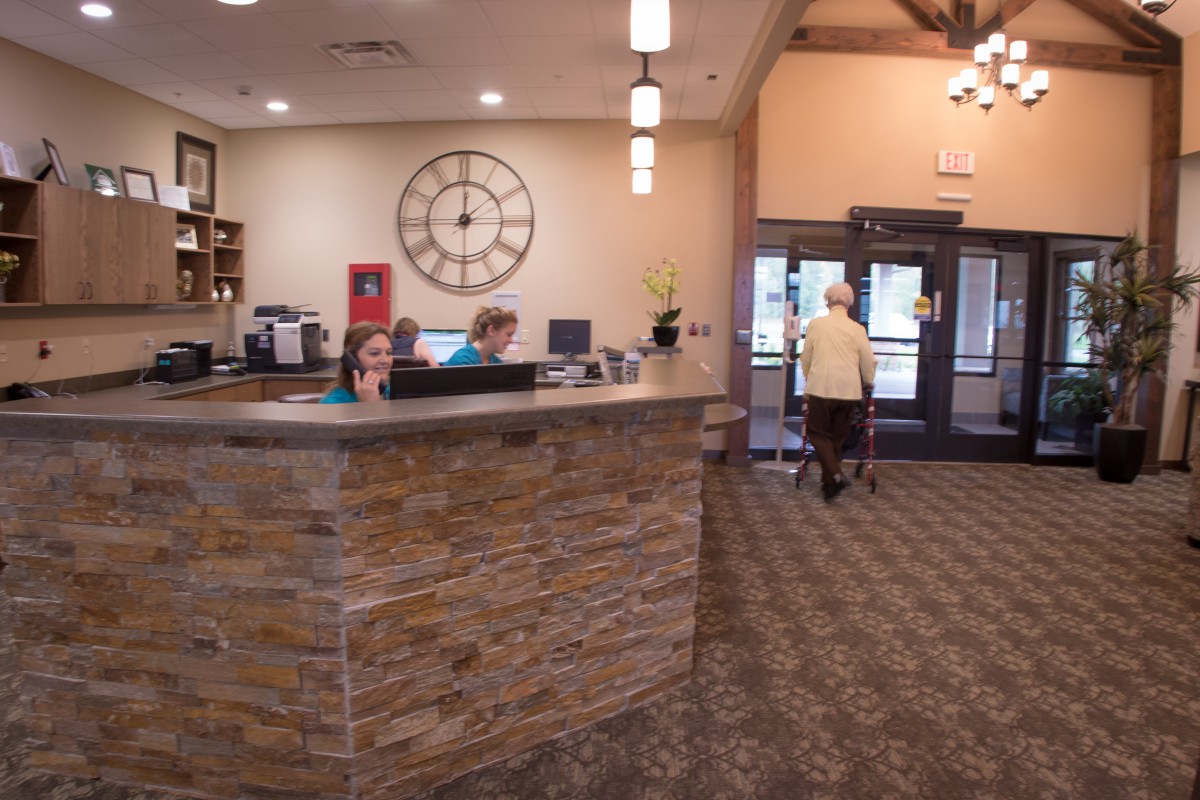 A reception area with a stone counter, a large wall clock, and people working at desks.