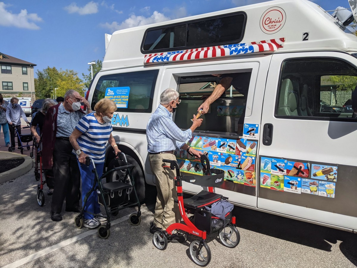 Elderly individuals enjoying ice cream from a truck on a sunny day.