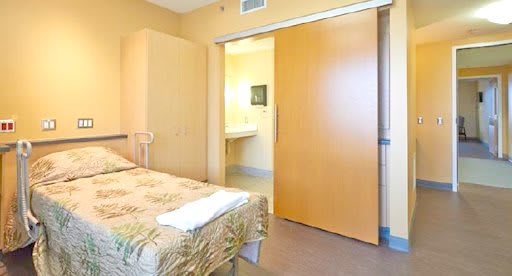 A modern hospital room with a single bed, featuring bright lighting and minimalist design.